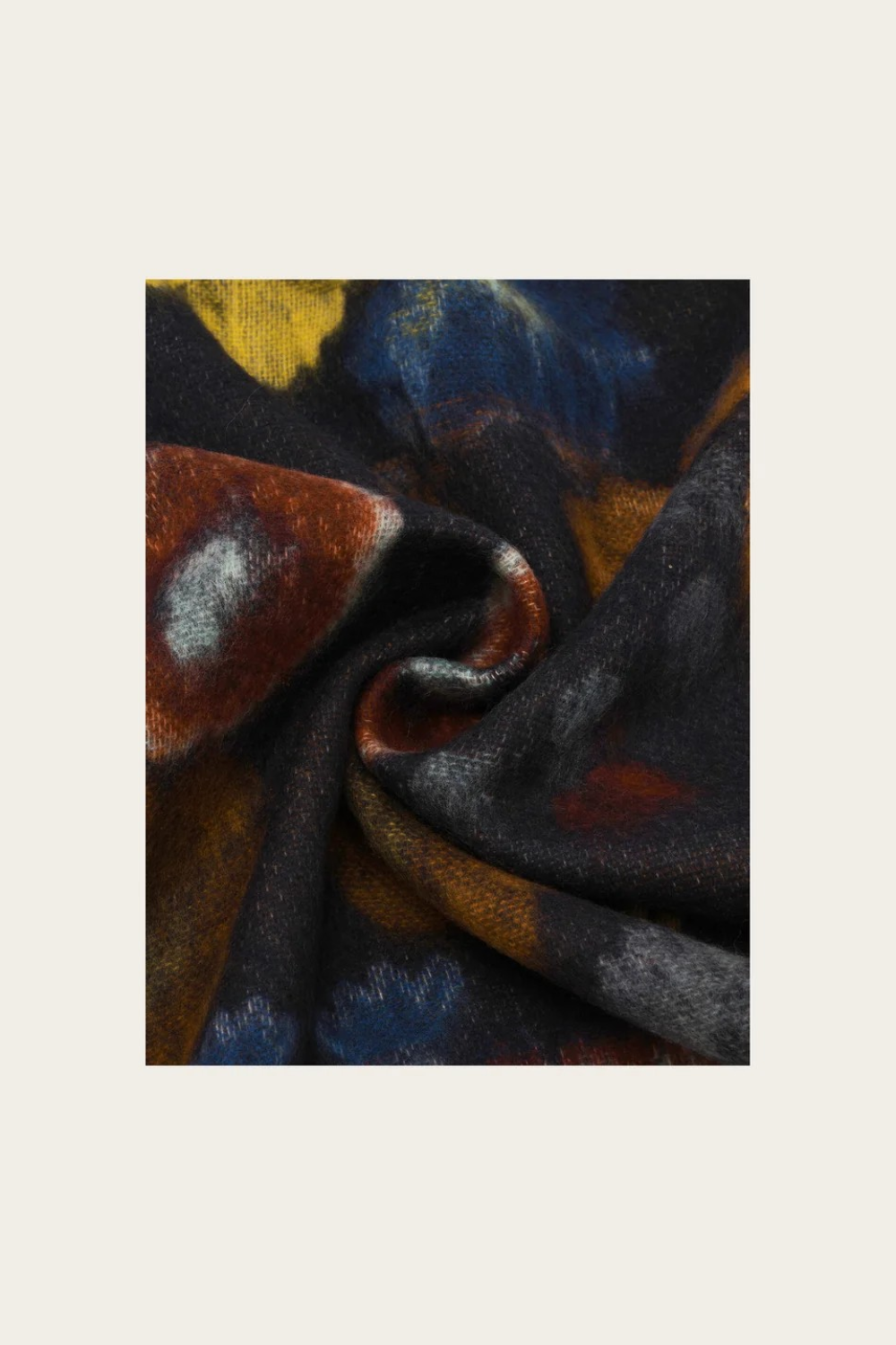 A close-up of draped fabric with an abstract painterly pattern in black, navy, blue, rust brown, ochre, and gray on a light beige background.