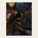 A close-up of draped fabric with an abstract painterly pattern in black, navy, blue, rust brown, ochre, and gray on a light beige background.