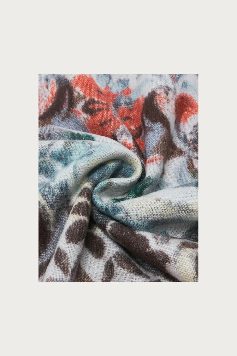 Close up of a  multi coloured floral scarf, with fringe, photographed against a light background.