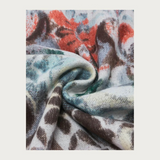 Close up of a  multi coloured floral scarf, with fringe, photographed against a light background.