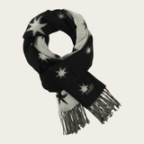 A black and white patterned scarf with star motifs and fringed ends, displayed on a light beige background.