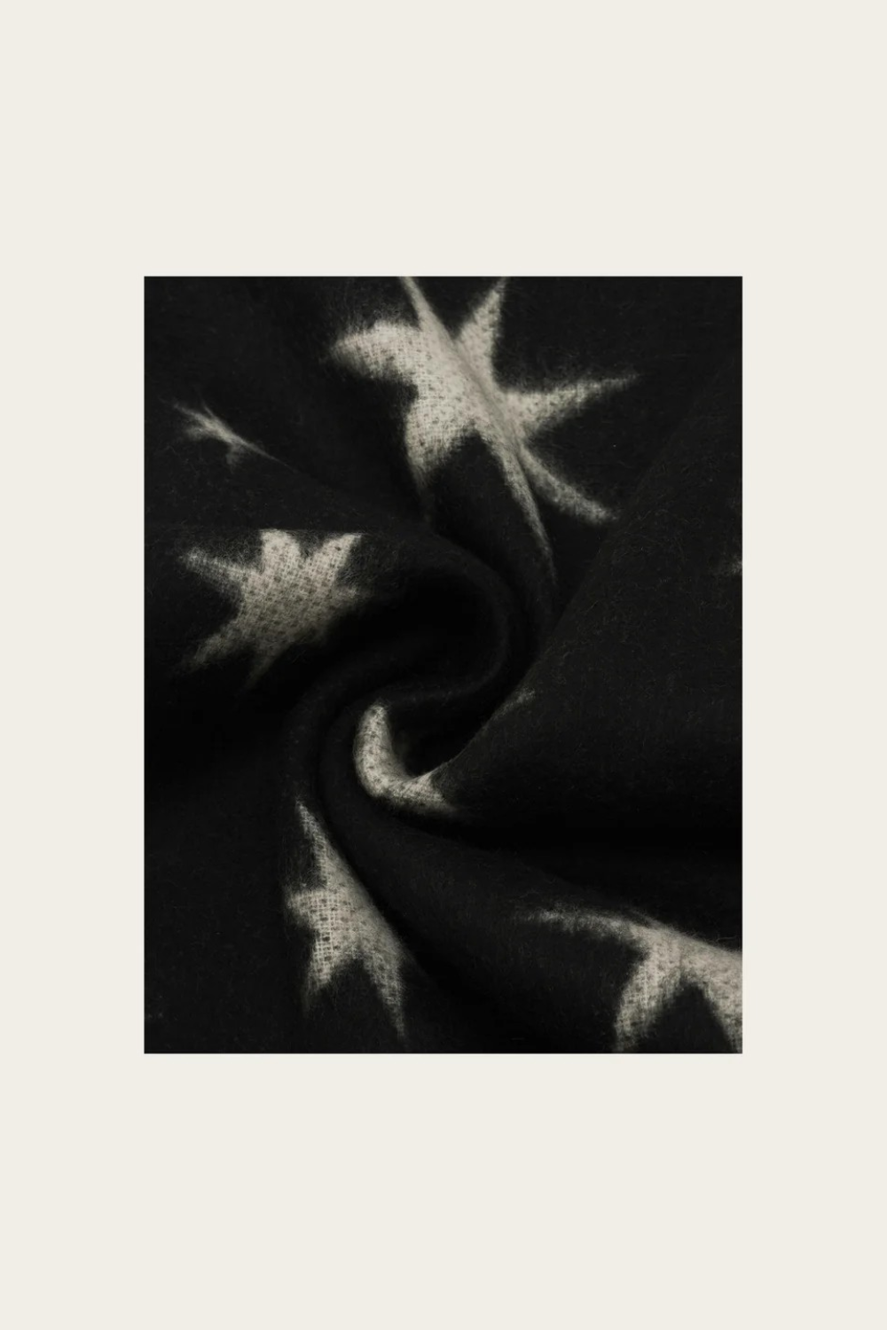 A close-up of a black knit fabric with a white star pattern, shown in a swirled drape against a light beige background.