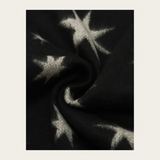 A close-up of a black knit fabric with a white star pattern, shown in a swirled drape against a light beige background.