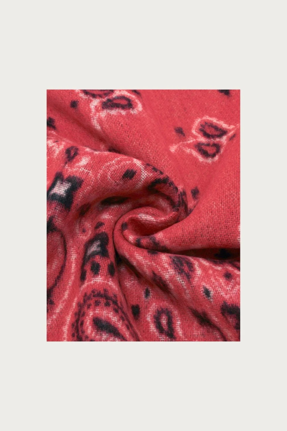 Close up of a red and grey paisley scarf photographed against a light background.