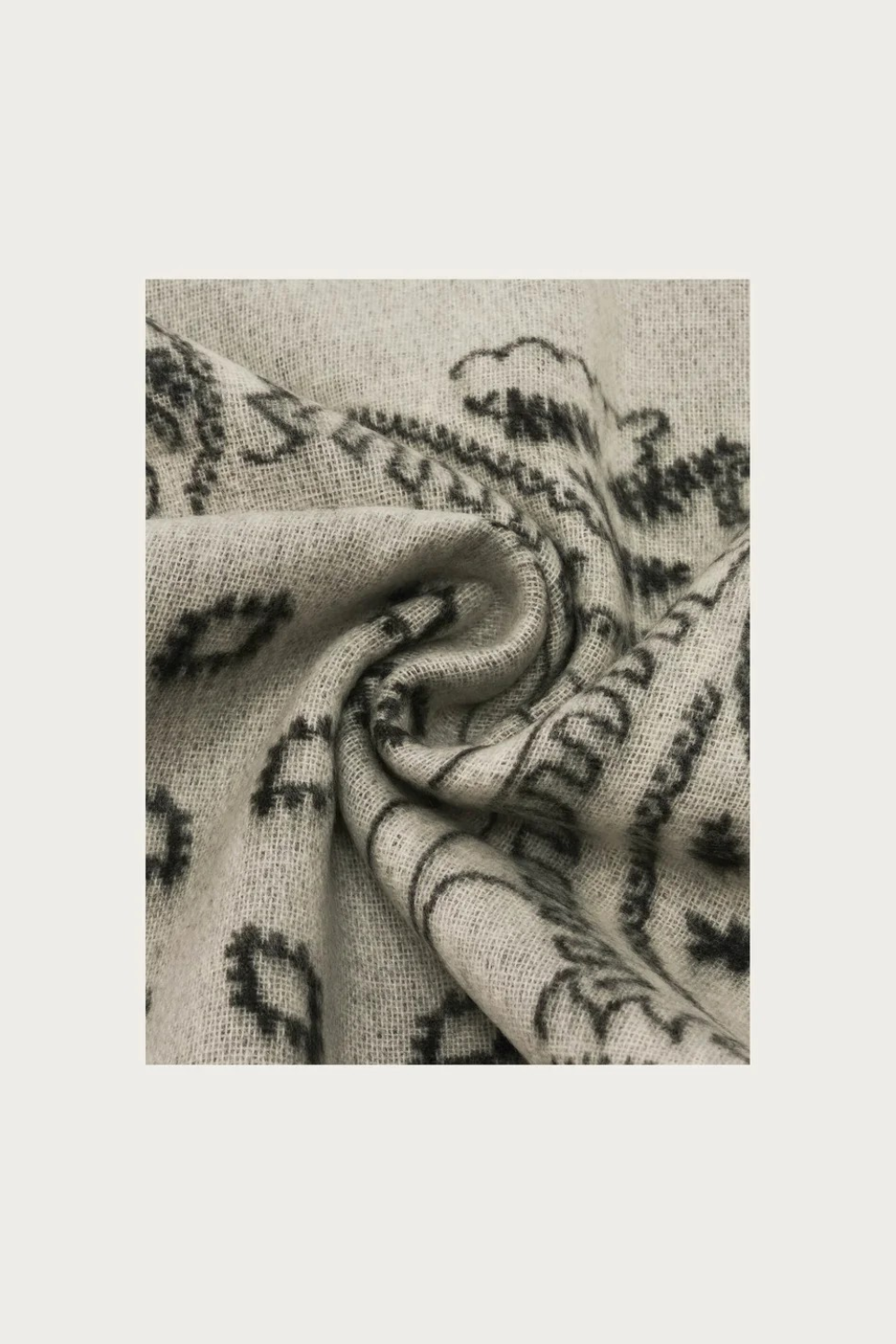 Close up of a grey and paisley scarf photographed against a light background.