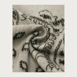 Close up of a grey and paisley scarf photographed against a light background.