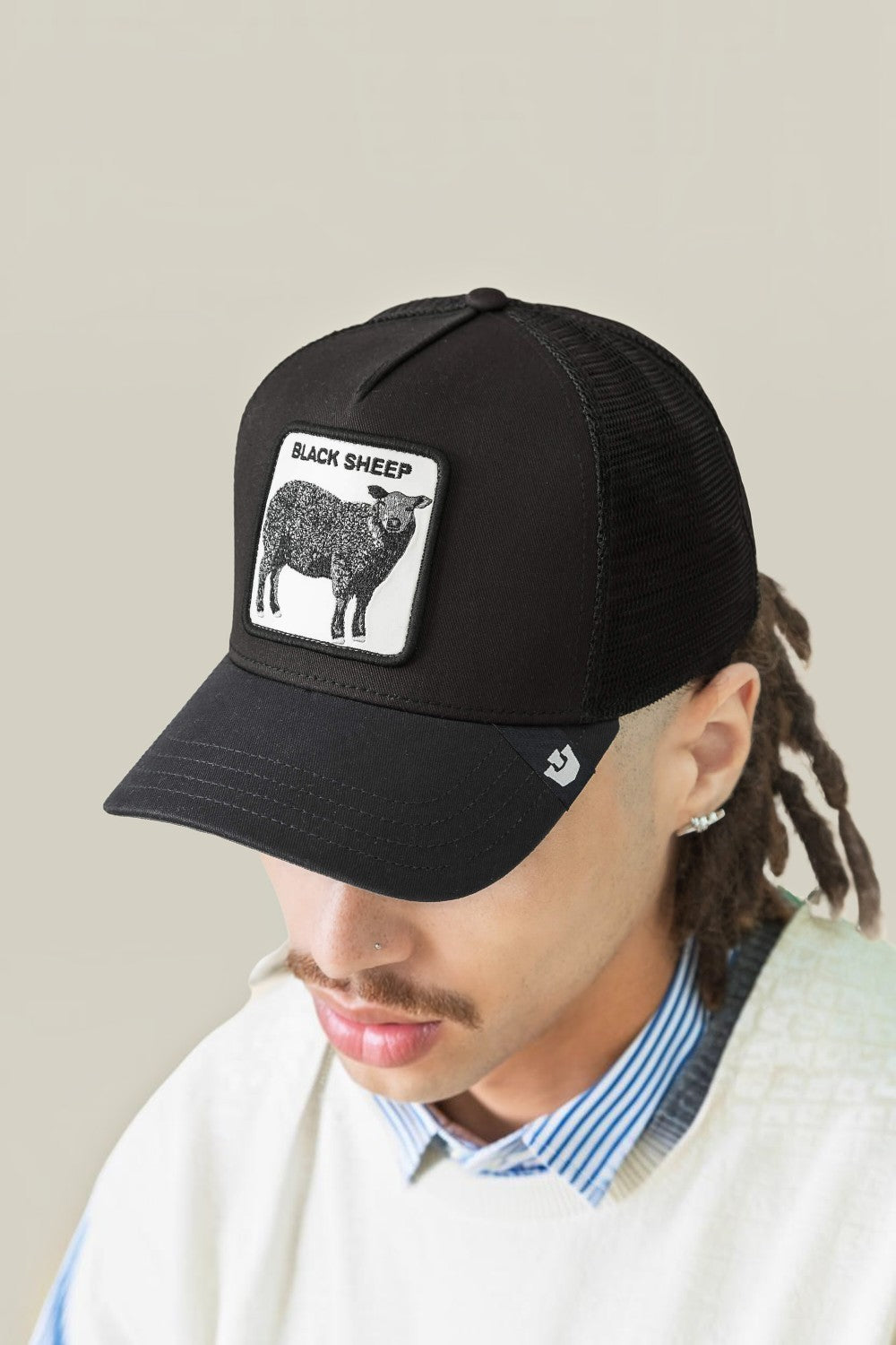 A man wearing a black trucker hat with a white rectangular patch featuring a black sheep illustration and the text 'BLACK SHEEP'.