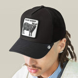 A man wearing a black trucker hat with a white rectangular patch featuring a black sheep illustration and the text 'BLACK SHEEP'.