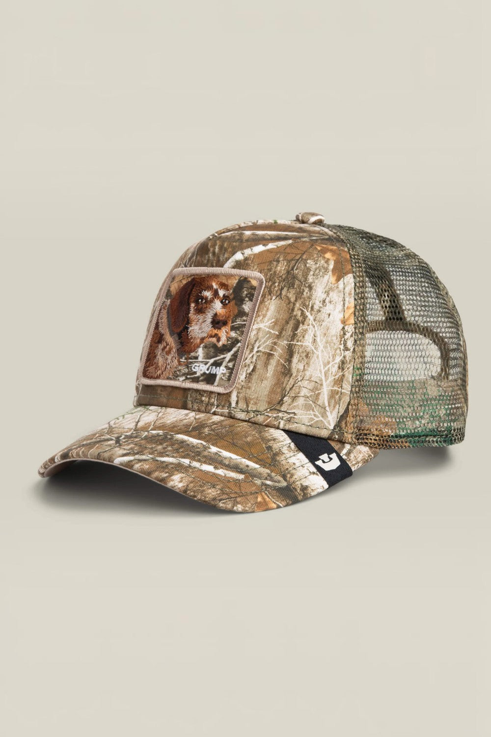 A camouflage trucker cap featuring a realistic dog portrait patch on the front panel and a black mesh back, set against a solid light beige background.