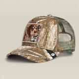 A camouflage trucker cap featuring a realistic dog portrait patch on the front panel and a black mesh back, set against a solid light beige background.