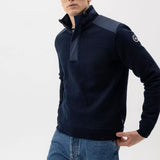 Man wearing a dark blue sweater with a high collar and jeans on a white background