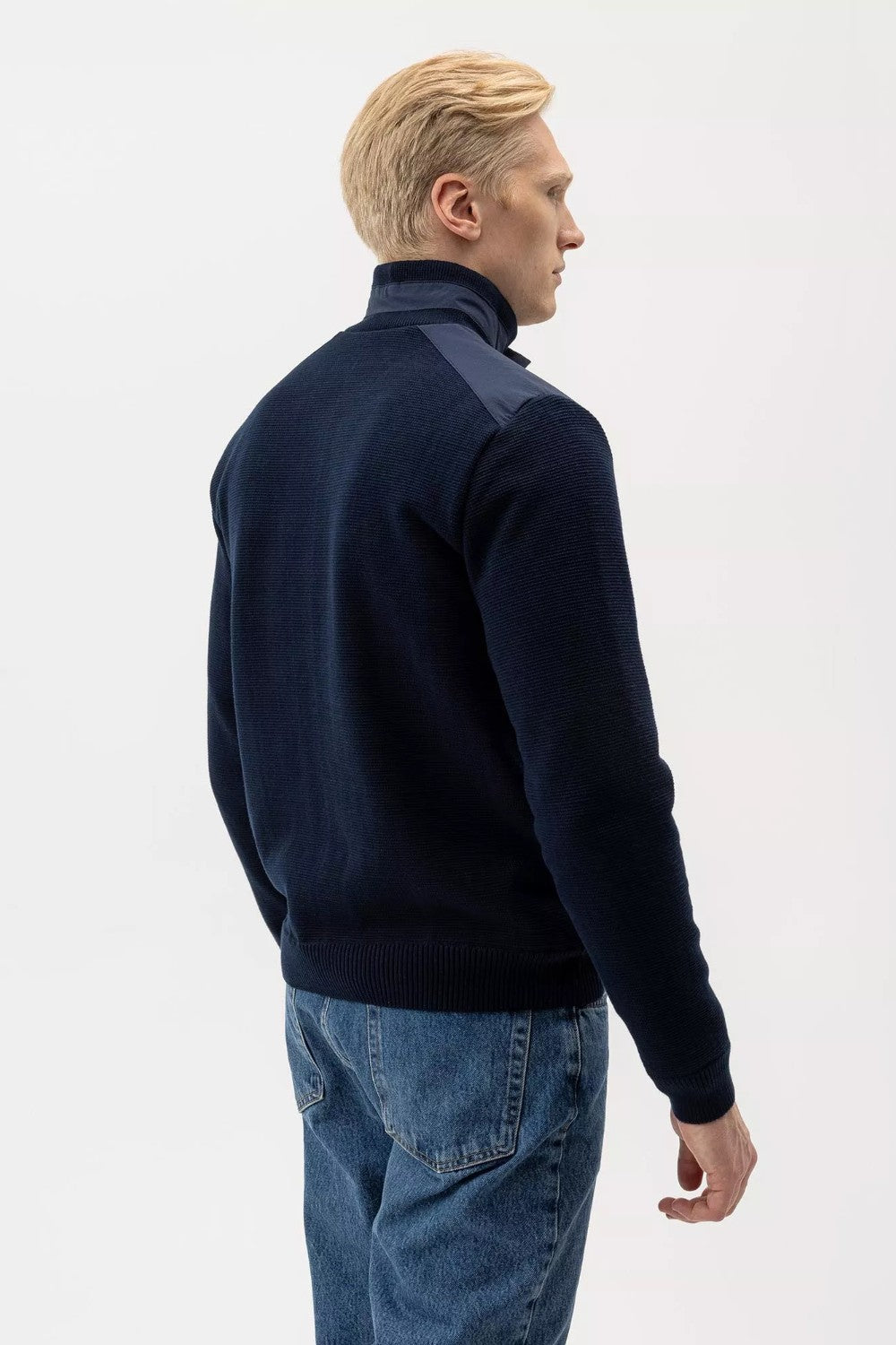 Man wearing a navy blue sweater and jeans on a white background