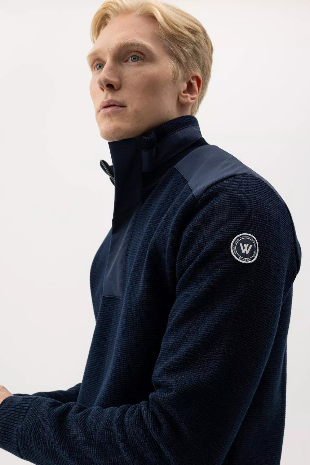 Man wearing a navy blue sweater with a logo on a white background