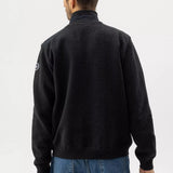 Man wearing a black jacket with a logo on the sleeve against a white background