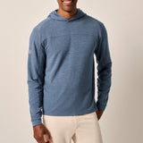Man wearing a blue hoodie and white pants against a beige background