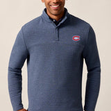 Man wearing a blue sweater with a logo on a beige background