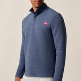 Man wearing a blue patterned pullover with a logo on a beige background
