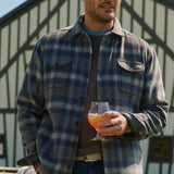 Man wearing a plaid shirt holding a glass of orange juice outdoors.
