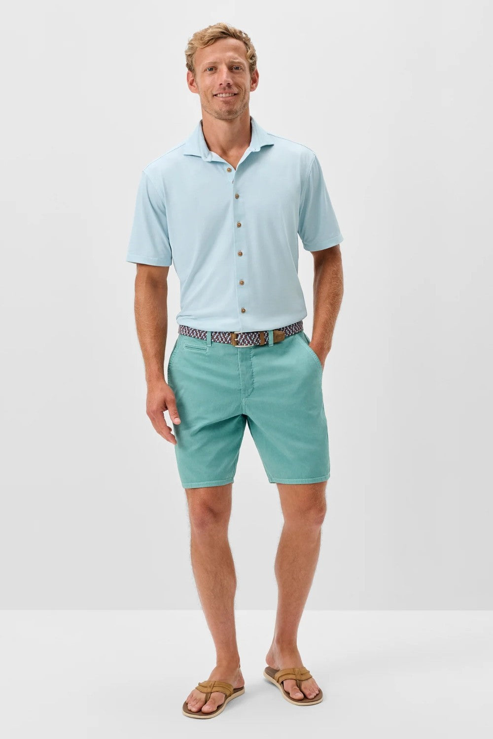 Man wearing a light blue polo shirt and green shorts on a white background