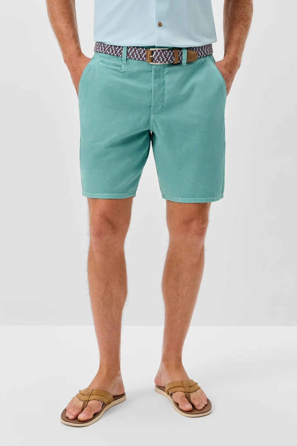 Person wearing teal shorts and a light blue shirt with a patterned belt on a white background