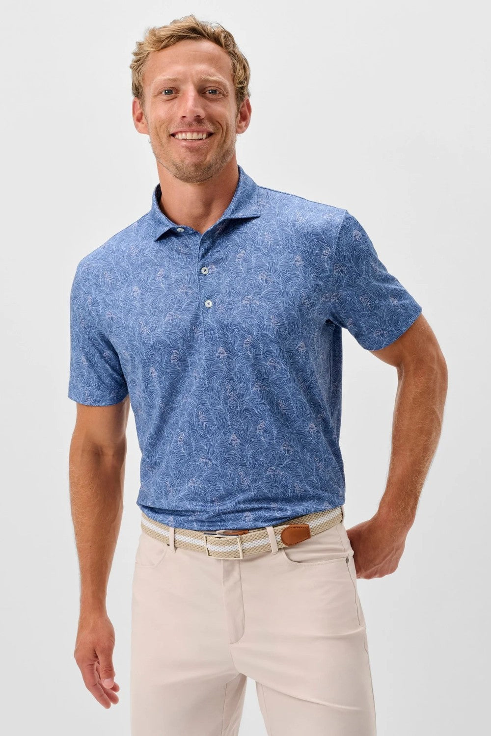 Man wearing a blue patterned polo shirt and beige pants on a light gray background