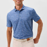 Man wearing a blue patterned polo shirt and beige pants on a light gray background