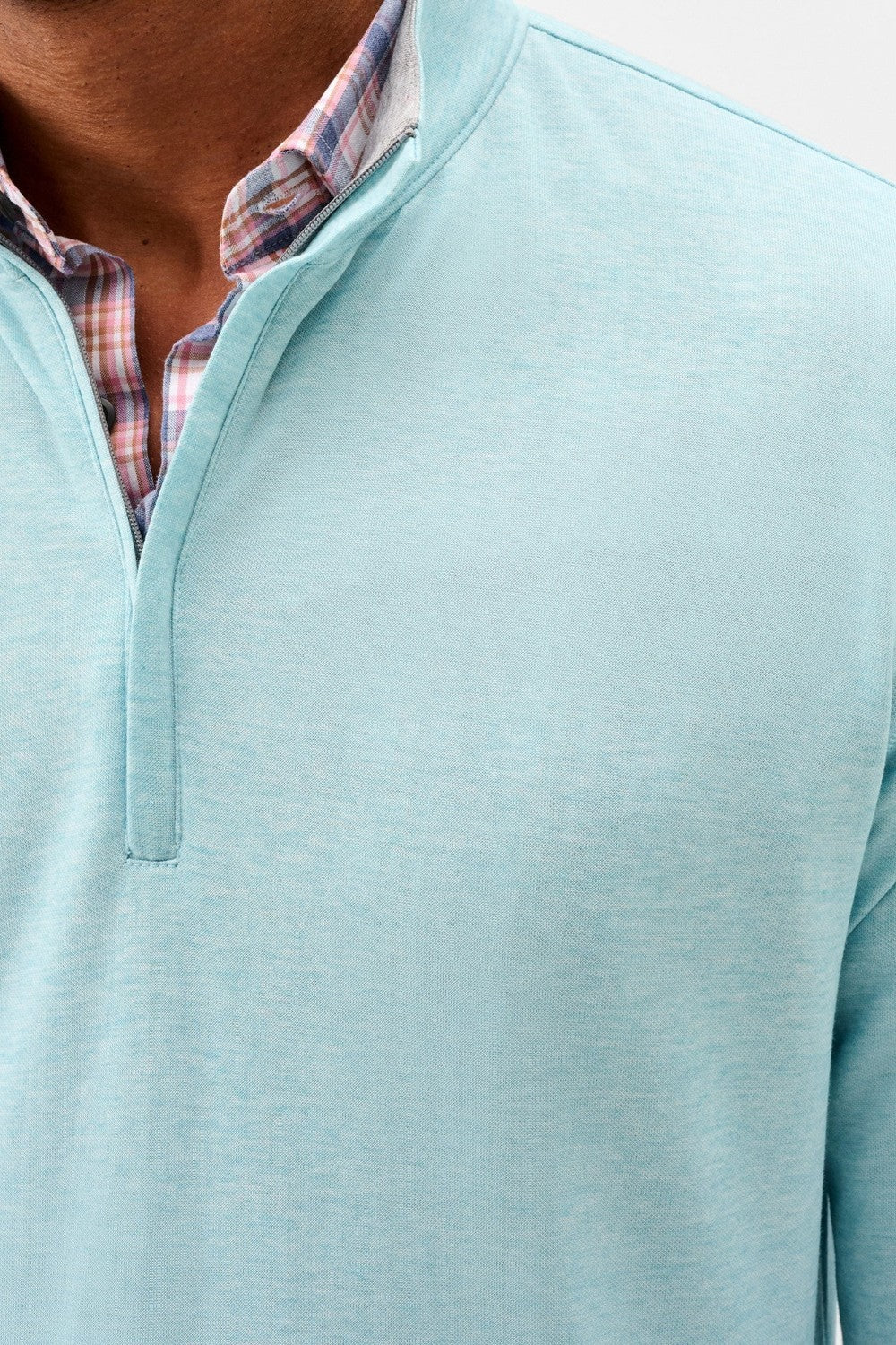 Close-up of a person wearing a light blue pullover with a plaid shirt underneath.