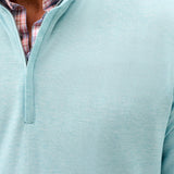 Close-up of a person wearing a light blue pullover with a plaid shirt underneath.