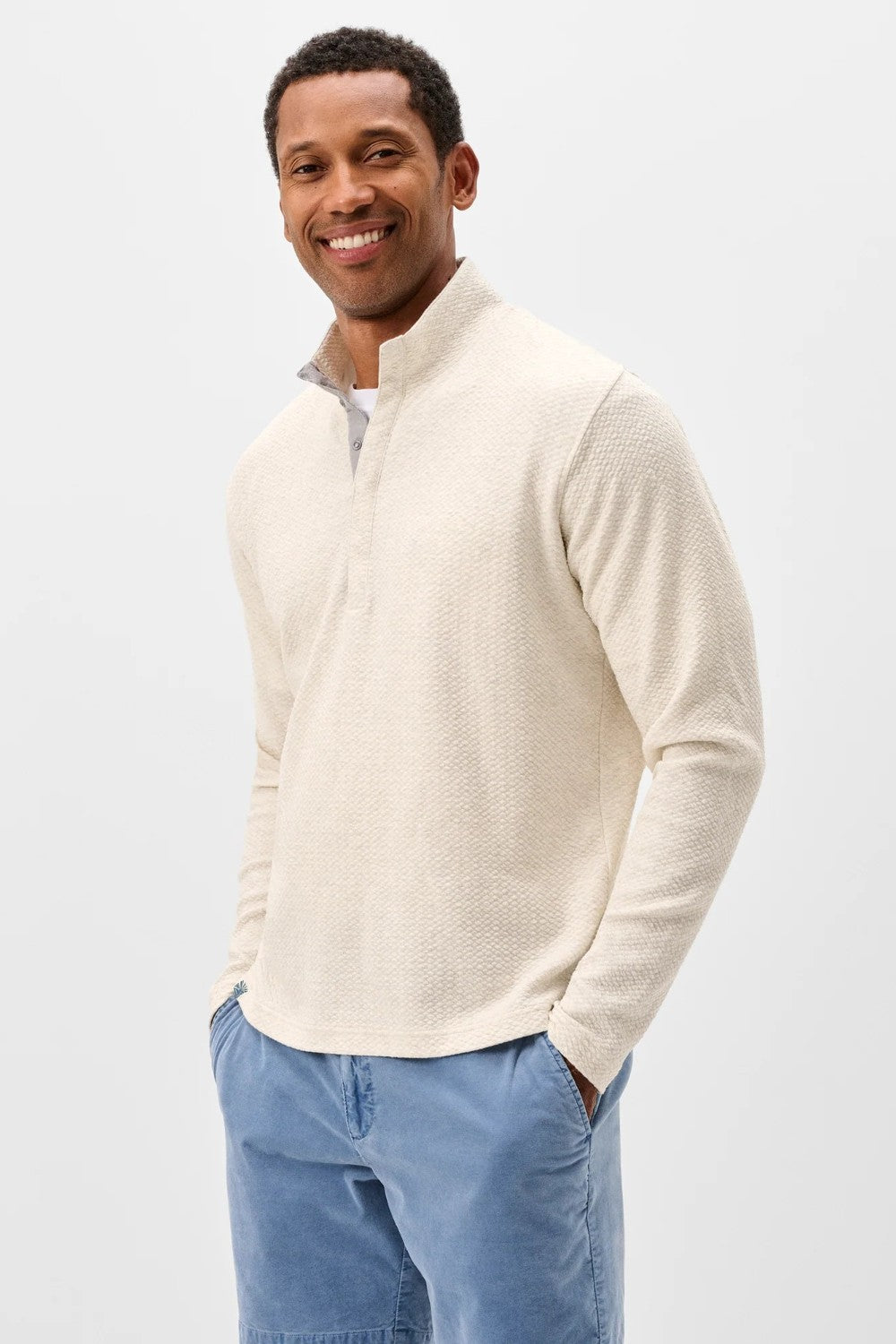 Man wearing a cream half-zip sweater and light blue pants on a white background
