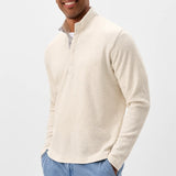 Man wearing a cream half-zip sweater and light blue pants on a white background