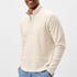 Man wearing a cream half-zip sweater and light blue pants on a white background