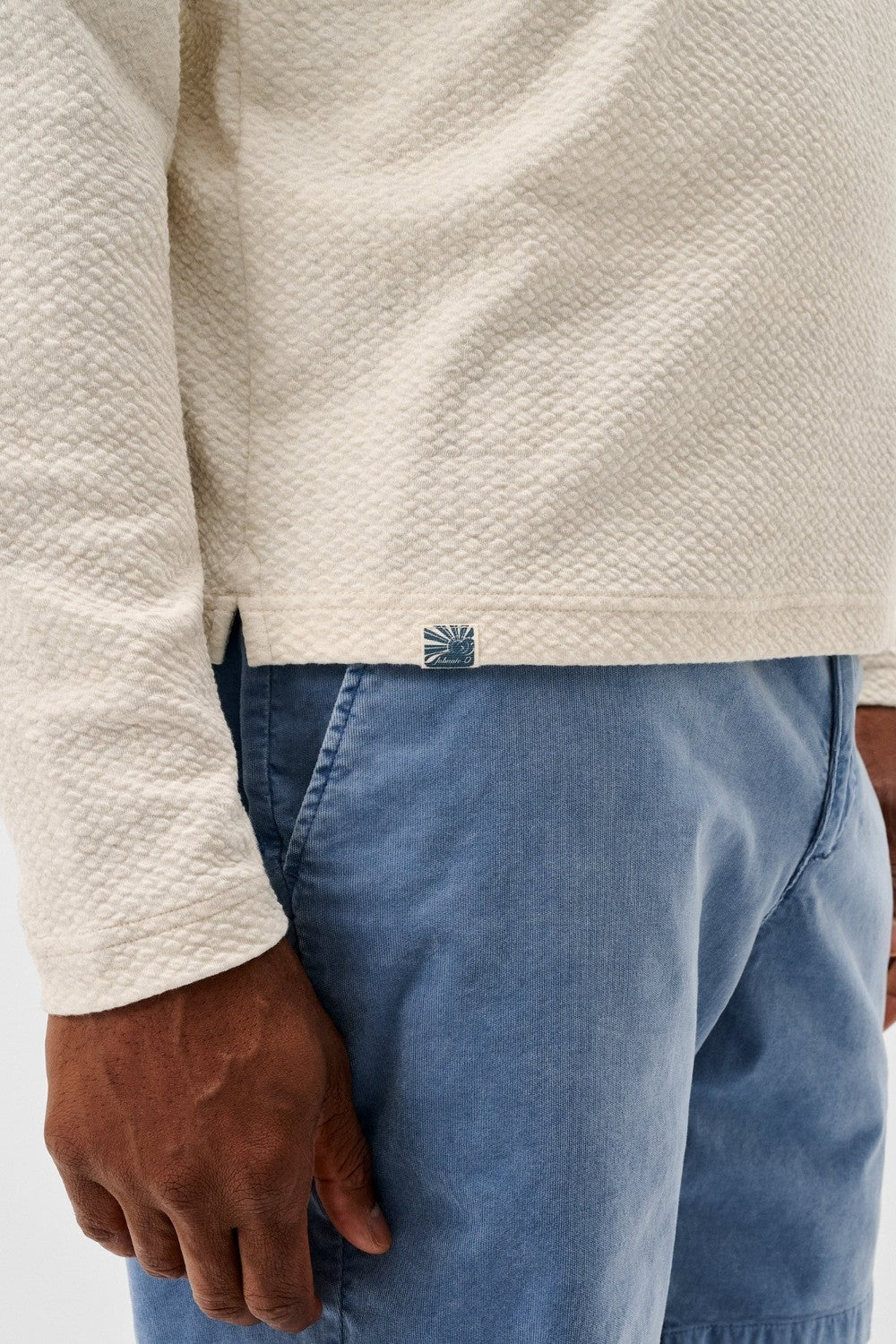 Person wearing a textured beige long-sleeve shirt and blue jeans with a visible brand logo.