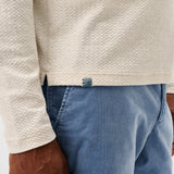 Person wearing a textured beige long-sleeve shirt and blue jeans with a visible brand logo.