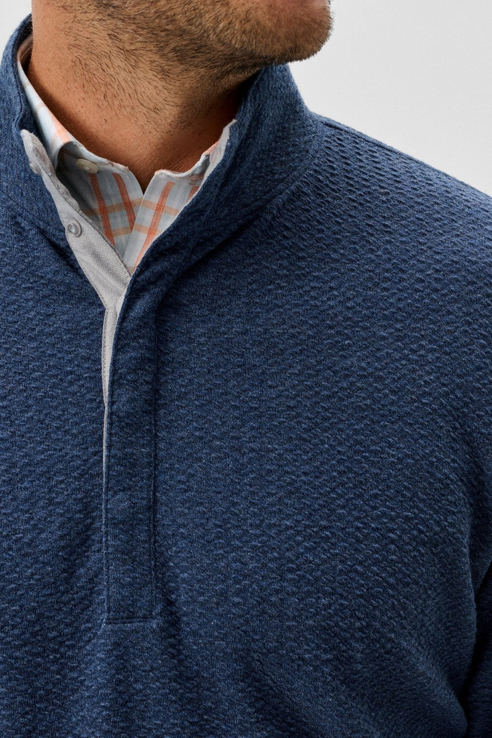 Close-up of a person wearing a blue textured sweater over a checkered shirt.