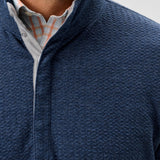 Close-up of a person wearing a blue textured sweater over a checkered shirt.
