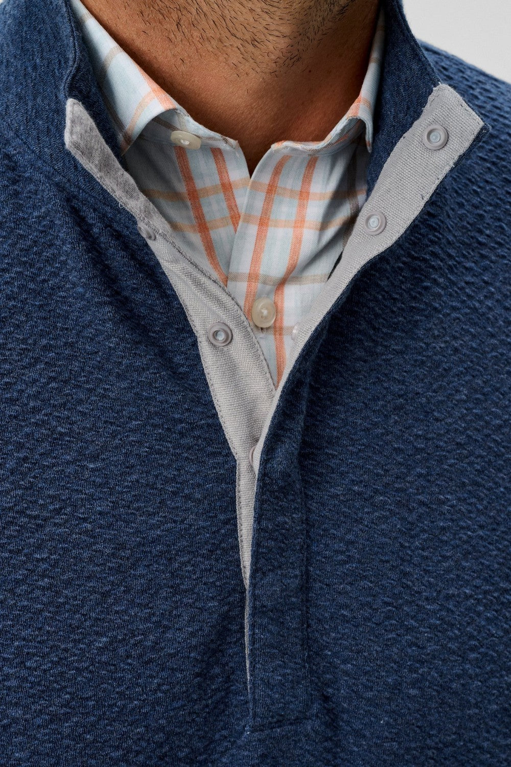 Close-up of a person wearing a navy blue sweater over a plaid shirt.