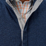 Close-up of a person wearing a navy blue sweater over a plaid shirt.