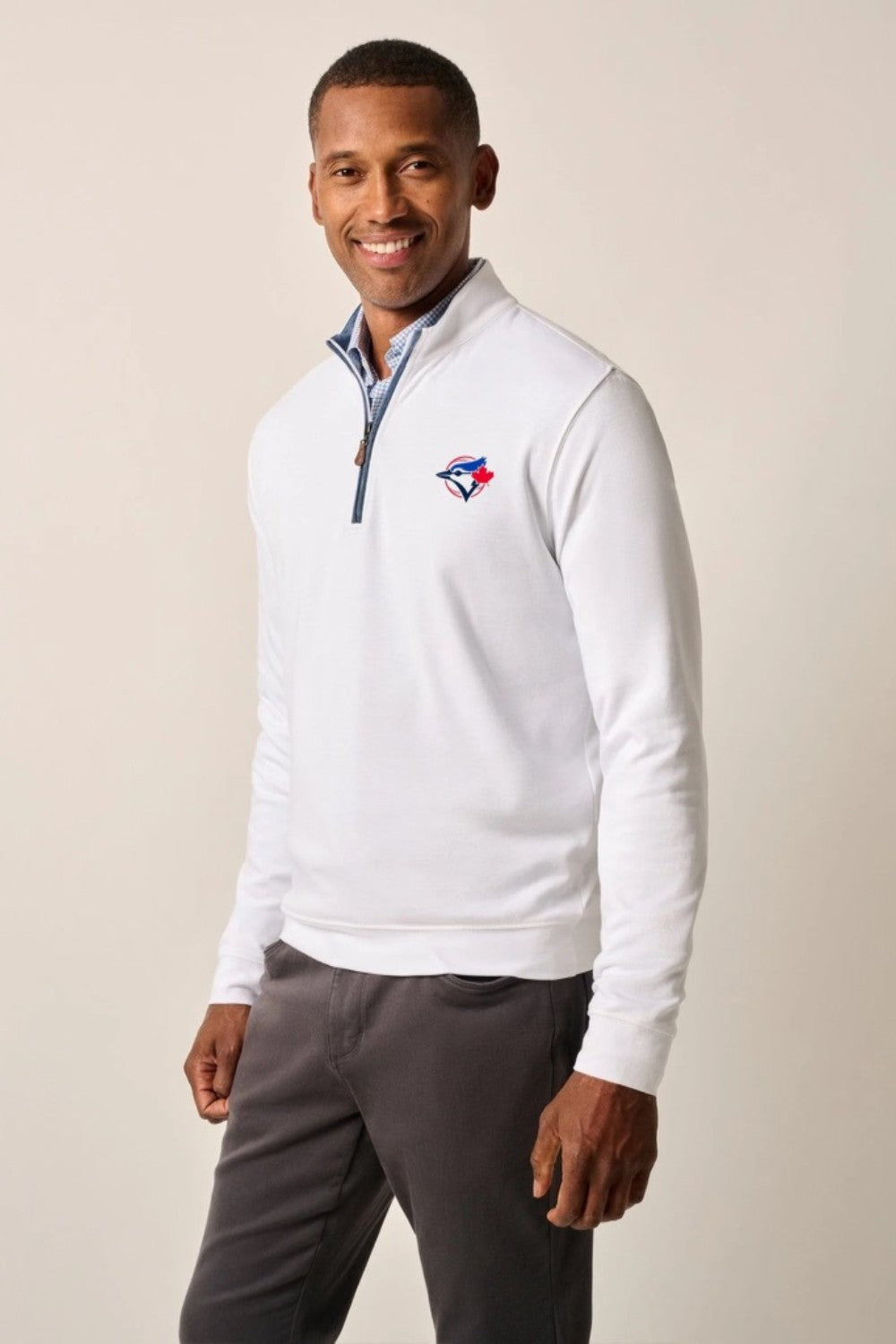 Man wearing a white quarter-zip pullover with a logo on a beige background