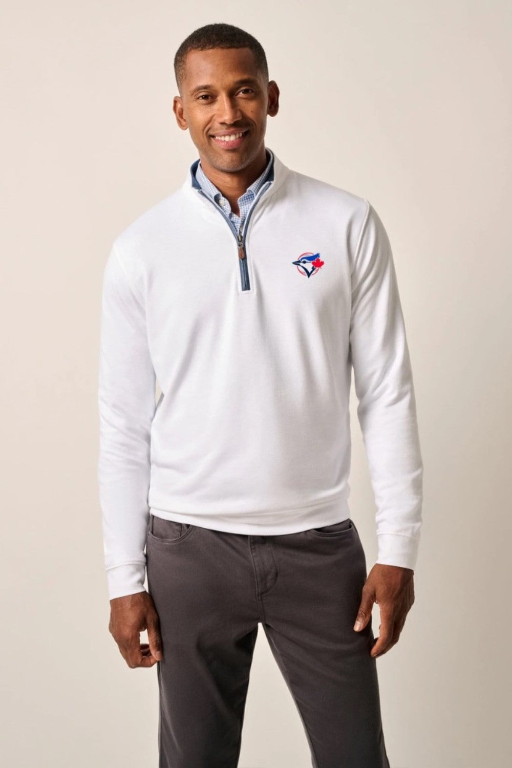 Man wearing a white quarter-zip pullover with a logo on a beige background