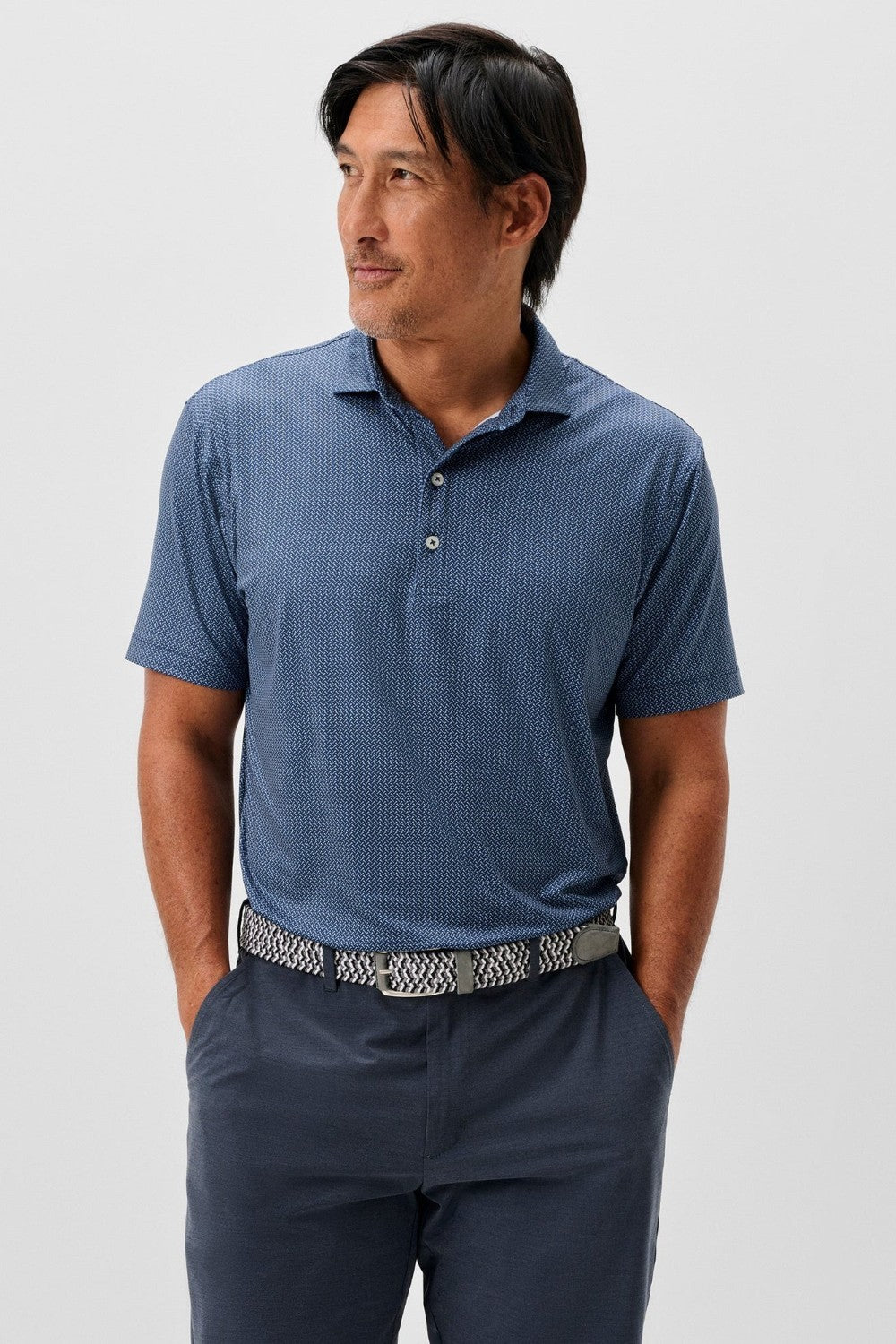 Man wearing a blue patterned polo shirt and dark pants on a white background