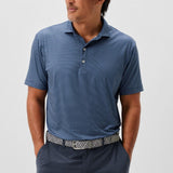 Man wearing a blue patterned polo shirt and dark pants on a white background