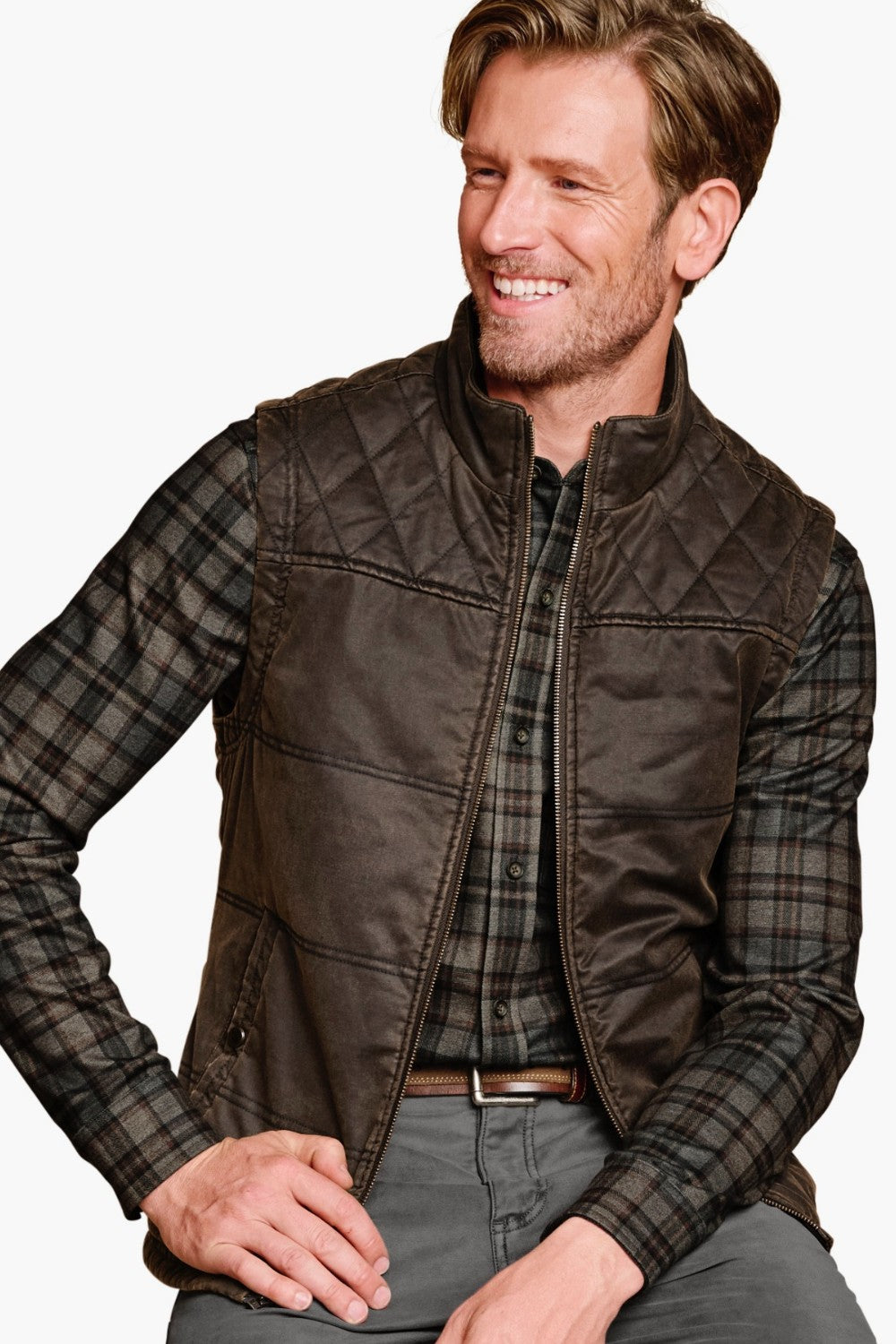 Man wearing a brown quilted vest over a plaid shirt on a white background