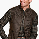 Man wearing a brown quilted vest over a plaid shirt on a white background