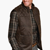 Man wearing a brown quilted vest over a plaid shirt on a white background
