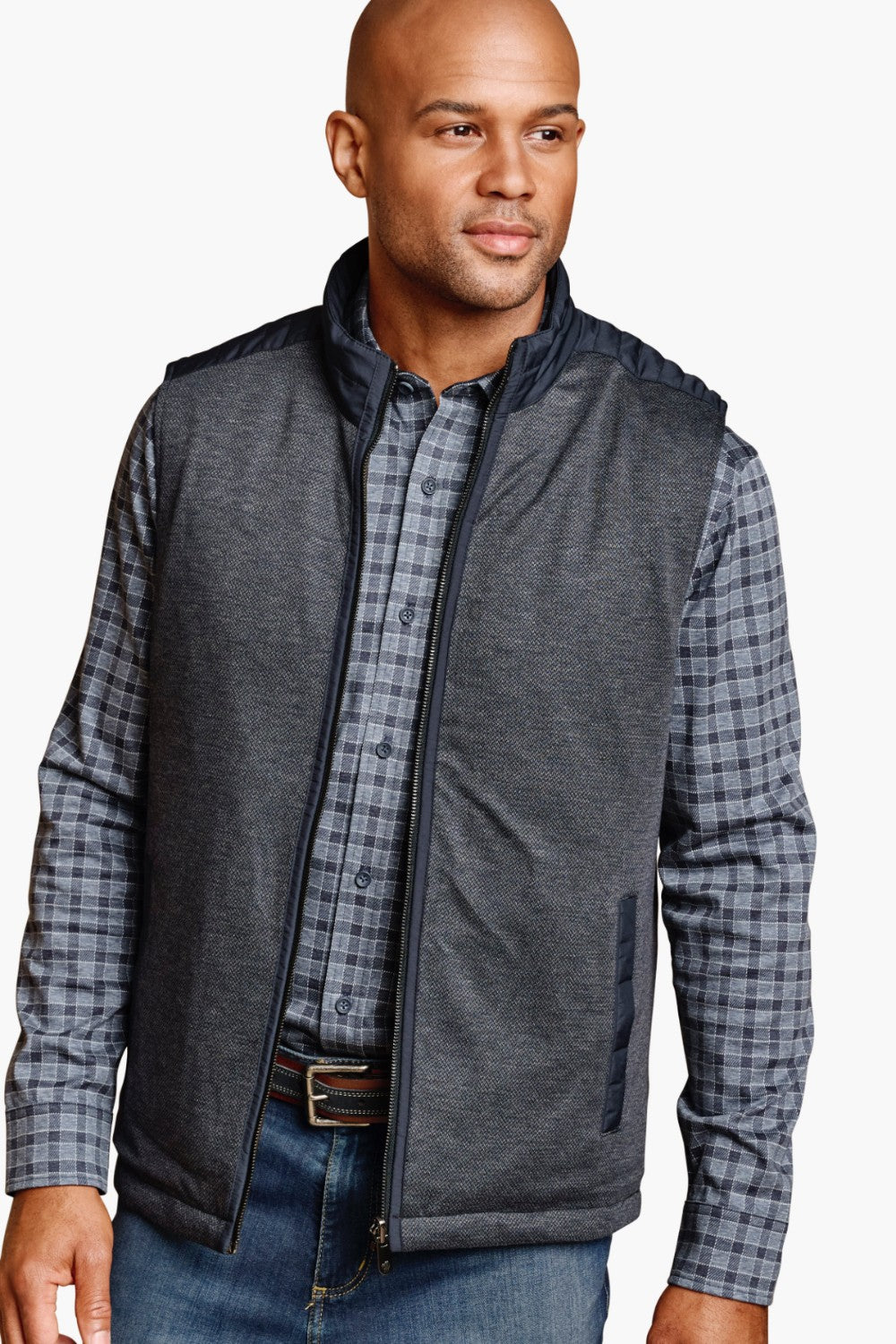 Man wearing a gray vest over a plaid shirt with a white background