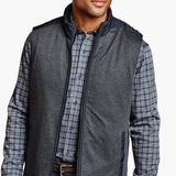 Man wearing a gray vest over a plaid shirt with a white background