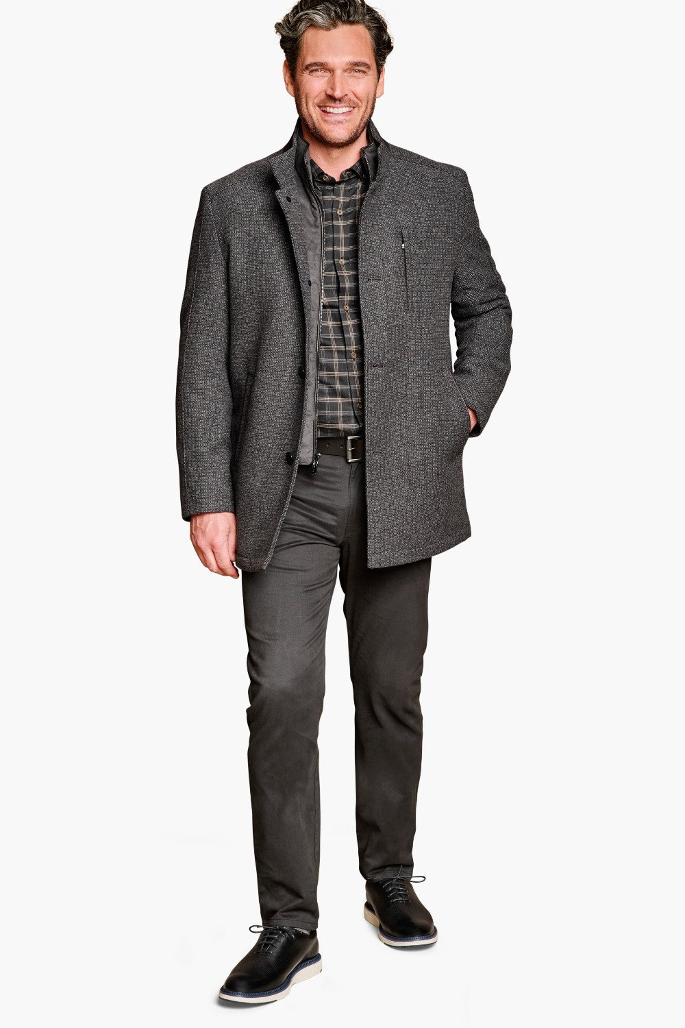 Man wearing a gray coat over a plaid shirt with gray pants on a white background