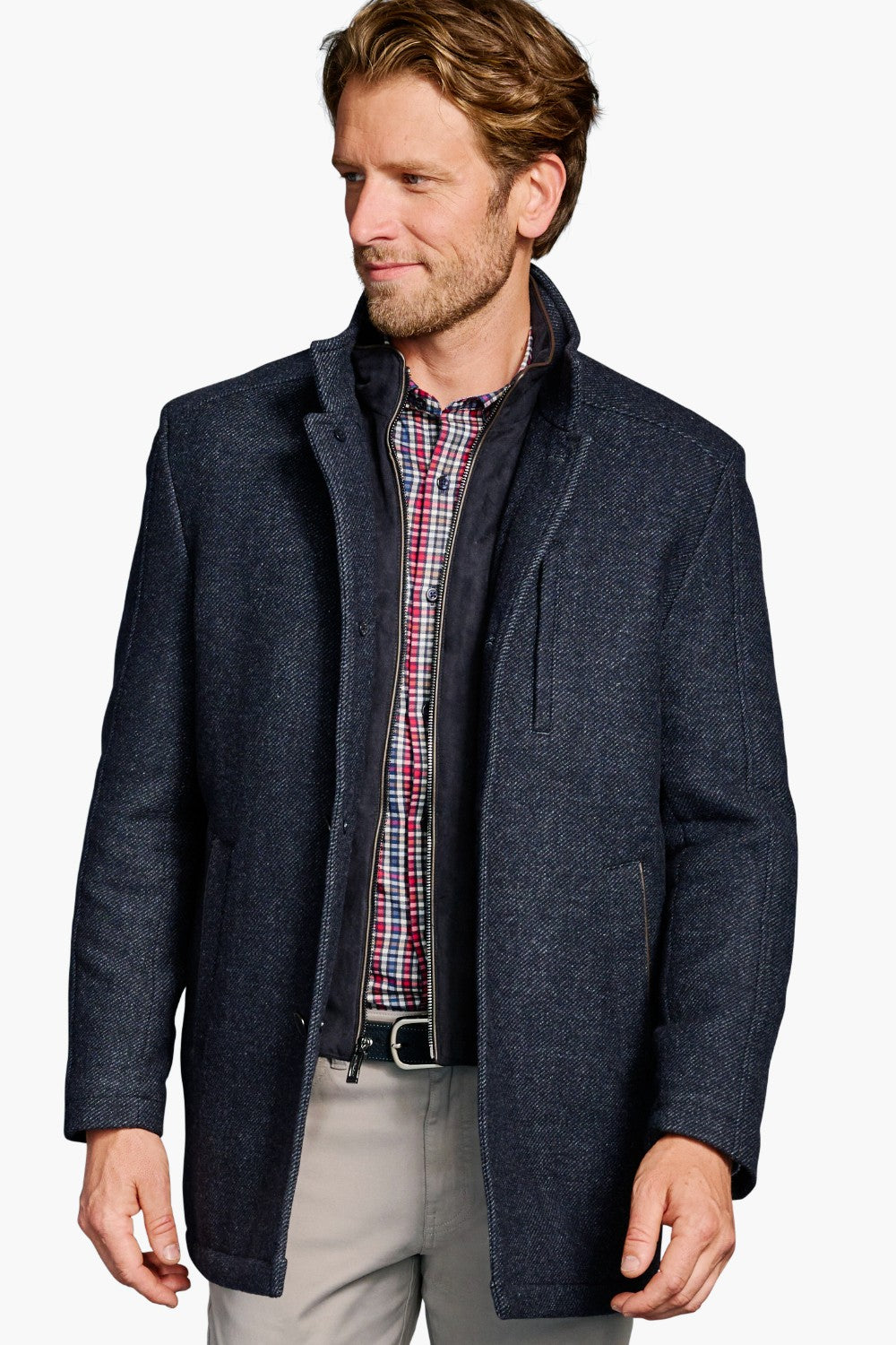 Man wearing a dark blue coat over a plaid shirt on a white background