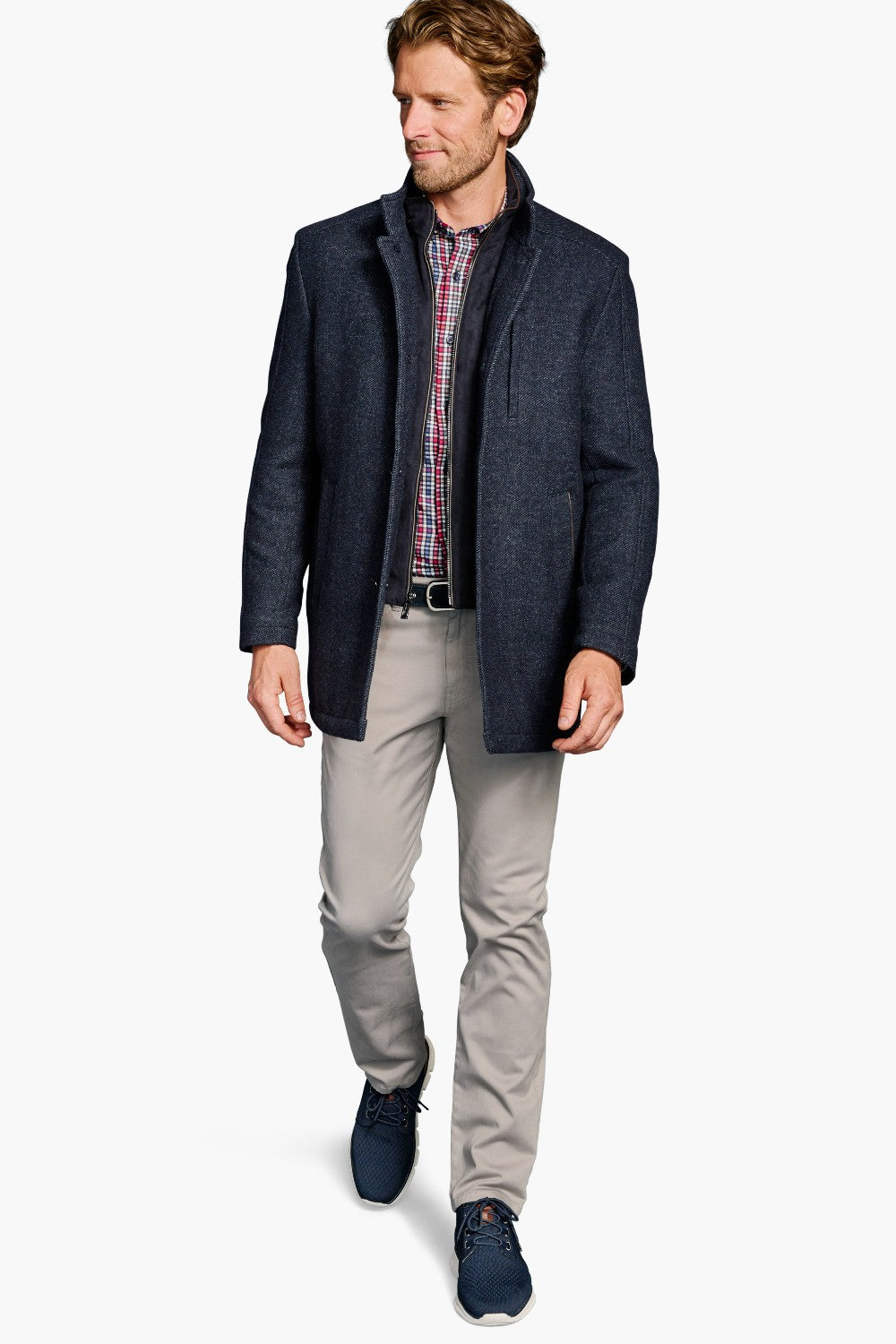 Man wearing a navy jacket, plaid shirt, and gray pants on a white background