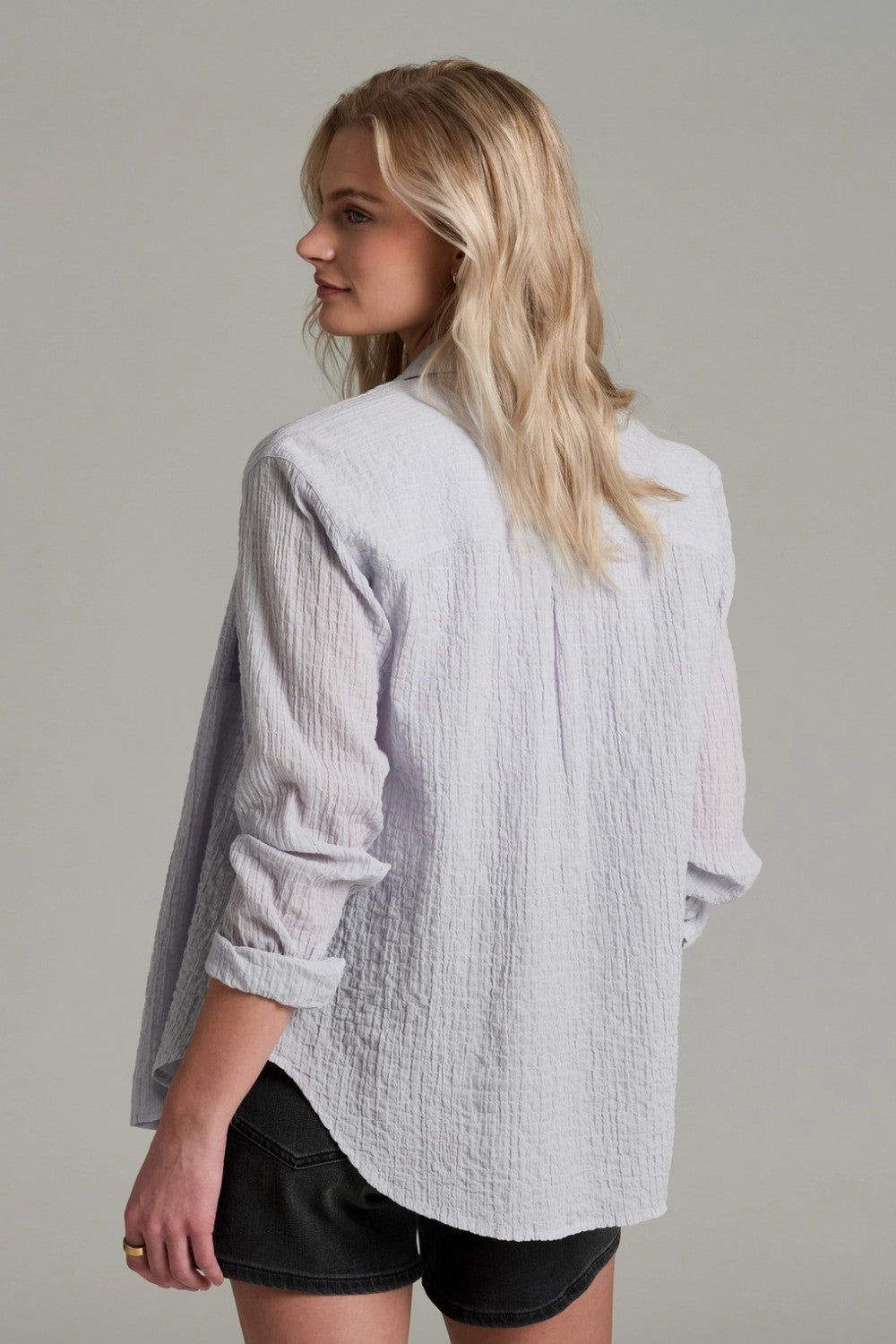 Woman wearing a light  textured shirt with rolled-up sleeves on a plain background